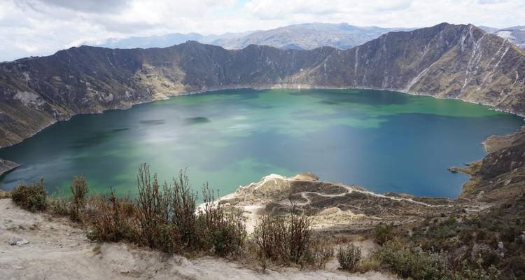 Panoramic view over the emerald waters of Quilotoa crater lake surrounded by steep volcanic walls.