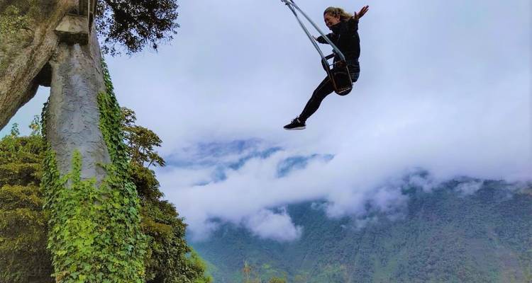 Adventurer soaring high on the cliffside swing above clouds and lush mountains near Baños.