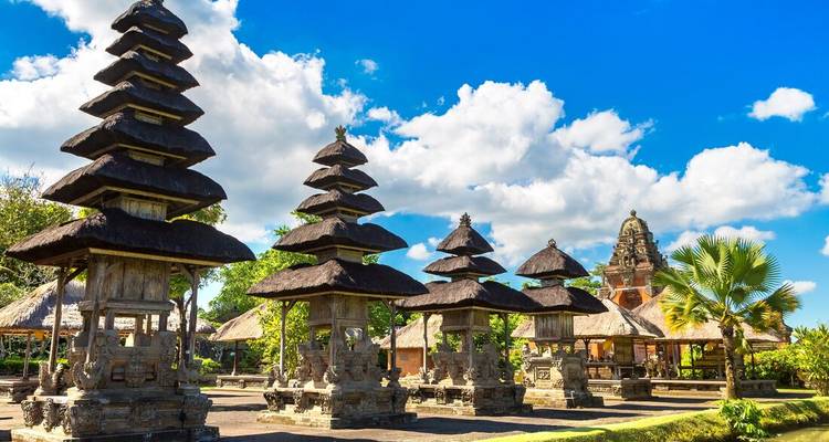 Series of multi-tiered pagoda shrines with thatched roofs set in a sunny Balinese temple garden.