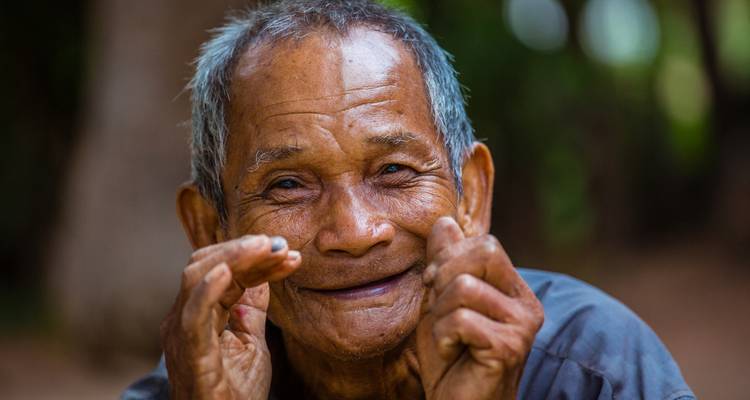 Retrato en primer plano de un hombre camboyano mayor sonriente con manos expresivas.