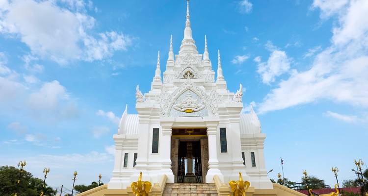 Elegant white Thai temple with multiple spires contrasts against a bright blue sky.