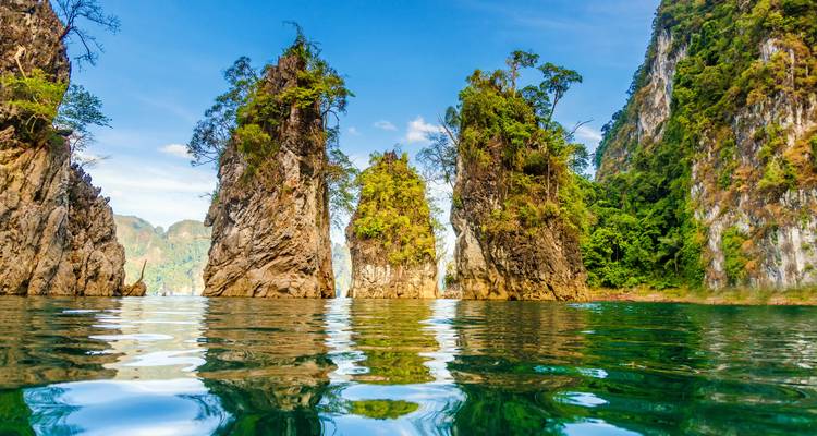 Jagged limestone karsts rise from emerald-green water in Khao Sok National Park.