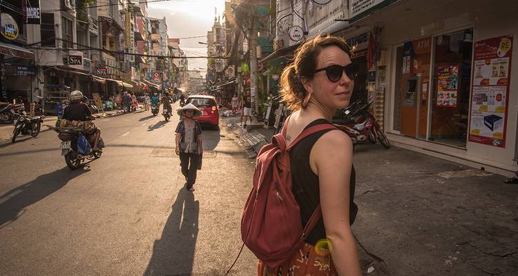 Femme avec un sac à dos regardant vers l'arrière en marchant le long d'une rue animée de la ville vietnamienne à l'heure dorée.