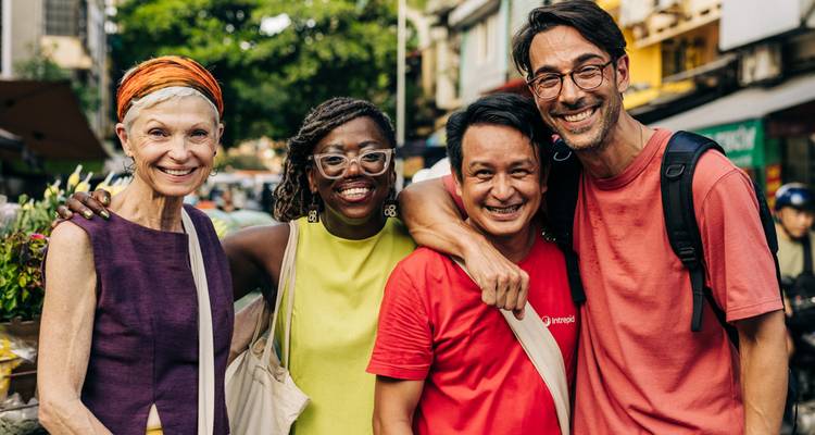 Quatre voyageurs heureux posent bras dessus, bras dessous dans un cadre de marché de rue animé.