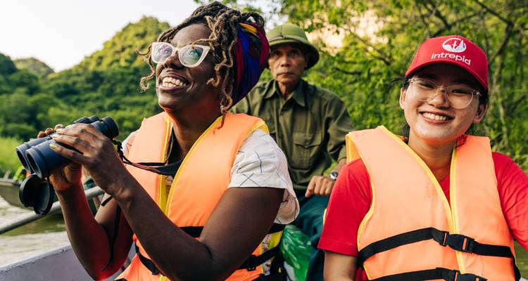 Les voyageurs vêtus de gilets de sauvetage de couleur vive sourient en observant les oiseaux depuis un petit bateau, avec des collines calcaires luxuriantes en arrière-plan.