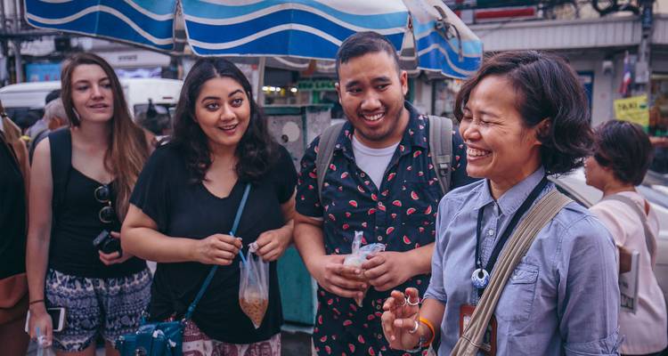 Smiling travellers sample street snacks under a blue striped awning during a city food tour.