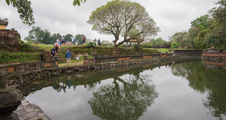 Visitors explore the moat and gardens of an historic Vietnamese citadel reflected in calm water.