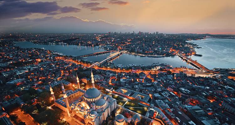 Vista aérea elevada al atardecer sobre el Cuerno de Oro de Estambul, con mezquitas iluminadas y puentes brillando contra el perfil de la ciudad.