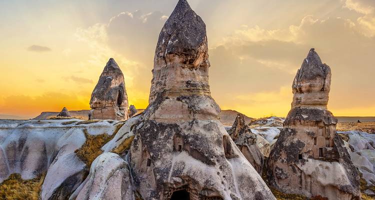Los picos de roca chimenea de hadas de Capadocia brillan con una suave luz dorada bajo un cielo pastel.