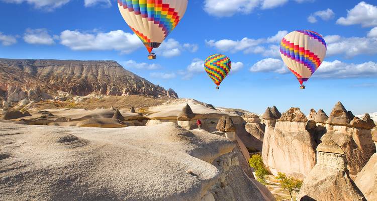 Los coloridos globos aerostáticos se deslizan sobre las distintivas formaciones rocosas de chimeneas de hadas de Capadocia bajo un cielo azul brillante.