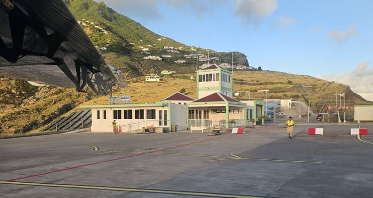 Klein eilandvliegveldterminal met bergachtig landschap op de achtergrond, gezien vanuit het vliegtuigraam.