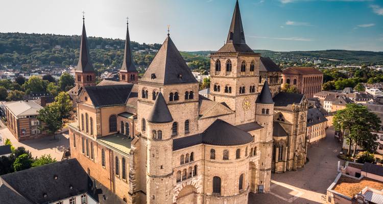 Aerial view of Trier Cathedral complex with distinctive Romanesque towers under bright sky.