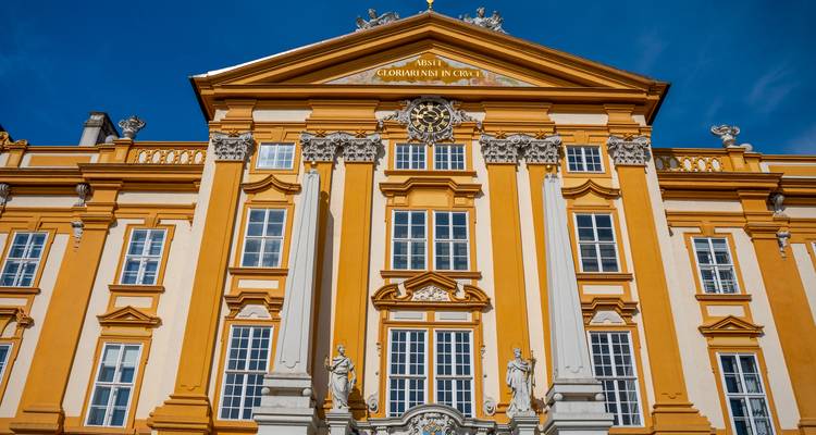 Ornate yellow façade of Melk Abbey with statues and baroque detailing under clear sky.