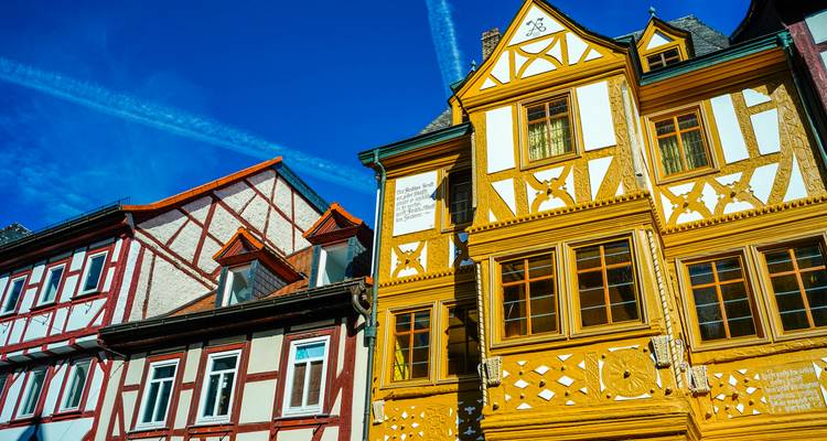 Colorful half-timbered German houses under rich blue sky streaked with jet trails.