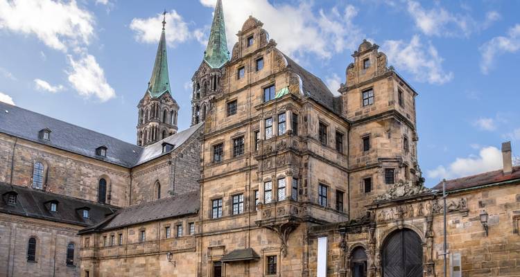 Stately sandstone palace complex crowned with twin green spires under a bright sky.