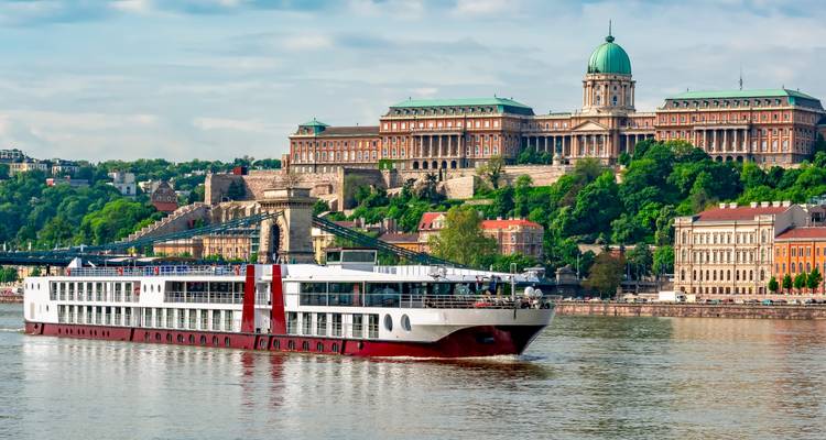 River cruise ship passing the Chain Bridge with Buda Castle and its green dome dominating the hilltop in Budapest.