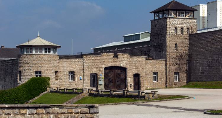 Stone walls, guard tower and entrance gate of the Mauthausen Memorial under a clear blue sky.