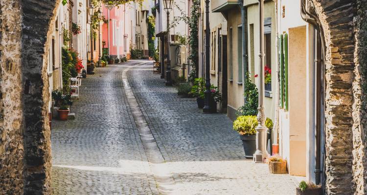 Charmante ruelle pavée étroite bordée de maisons historiques colorées, de plantes en pot et d'arcades baignées par la lumière chaude de l'après-midi.
