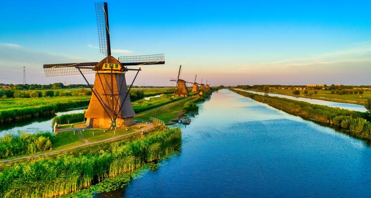 Lumière du soir vue du ciel au-dessus d'une rangée de moulins à vent hollandais traditionnels bordant un canal aux eaux réfléchissantes