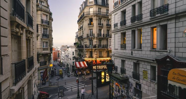 Rue parisienne étroite et animée à Montmartre bordée de cafés, de boutiques et d'une enseigne Metropol lumineuse au crépuscule