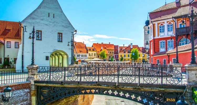 Colorful medieval houses and ornate wrought-iron Bridge of Lies over a stone arch in Sibiu’s old town square.