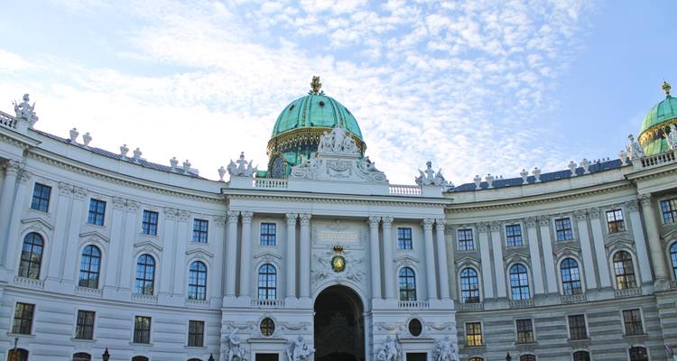 Close-up van de ingang van het Hofburg Palace met koepeldak en standbeelden tegen een licht bewolkte lucht.