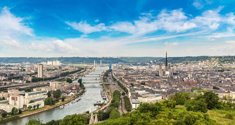Sweeping view over Rouen with the Seine River, bridges, and cathedral spire under a vivid blue sky.
