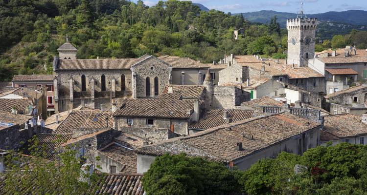 Panorama depuis les toits d'un village provençal médiéval avec église en pierre et collines boisées au-delà.