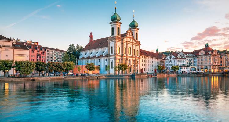 Avondlicht baadt de Jezuïetenkerk van Luzern en kleurrijke waterkanthuizen die weerspiegeld worden in de rivier de Reuss.
