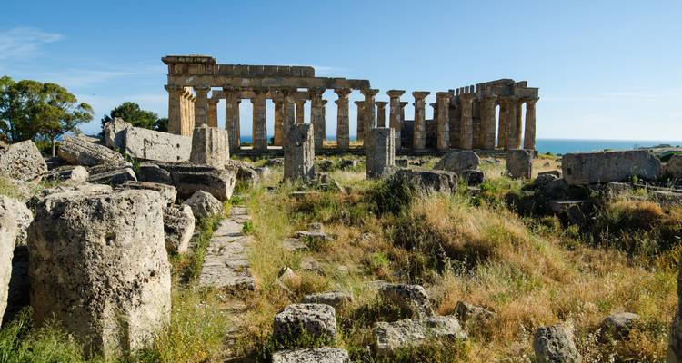 Les anciennes colonnes de pierre et les ruines s'étendant sur un terrain herbeux sous un ciel bleu