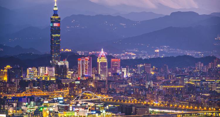 Panorama nocturne de la ville de Taipei avec la Taipei 101 illuminée sur fond de chaîne de montagnes.