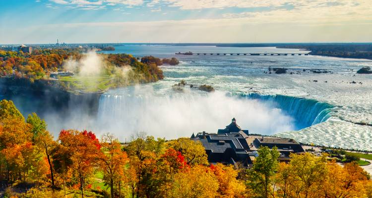 Spectacular aerial of Horseshoe Falls pouring mist over vibrant autumn foliage and river islands.