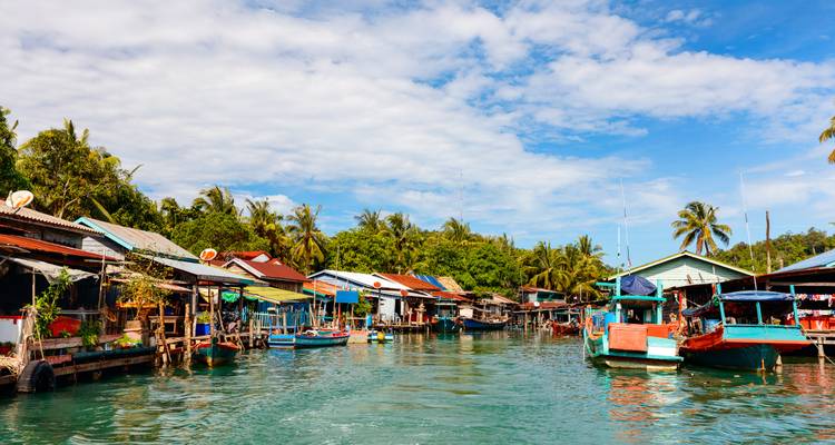 Des maisons colorées sur pilotis en bois et des bateaux de pêche alignés le long d'un calme chenal fluvial tropical.