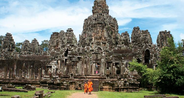 Deux moines en robes orange passent devant un imposant temple en pierre de style Bayon
