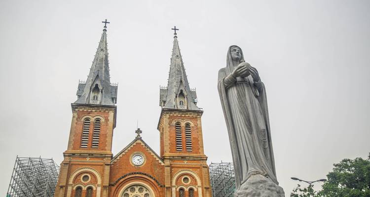 Twin spires of Notre-Dame Cathedral Basilica stand tall beside a statue under a pale sky.