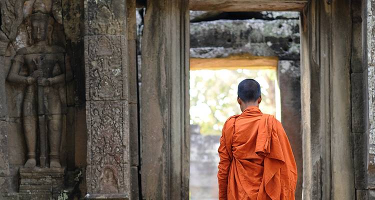 Moine vêtu de robes orange franchissant une porte en pierre illuminée par le soleil d'un ancien temple.