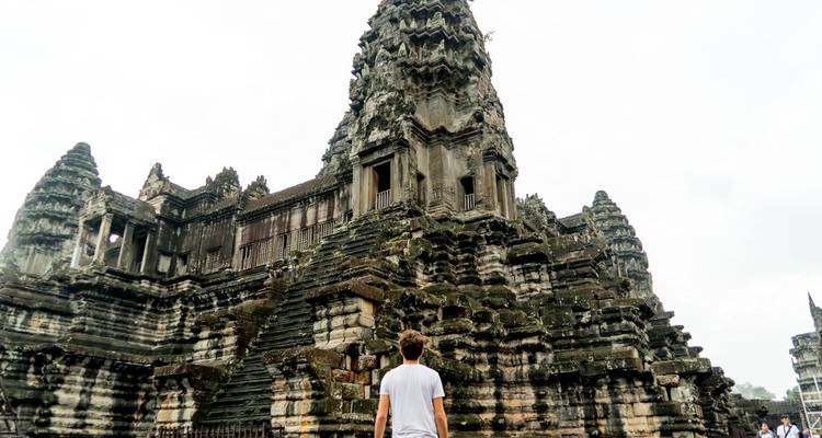 Traveler gazes up at the towering central spire of Angkor Wat on an overcast day.
