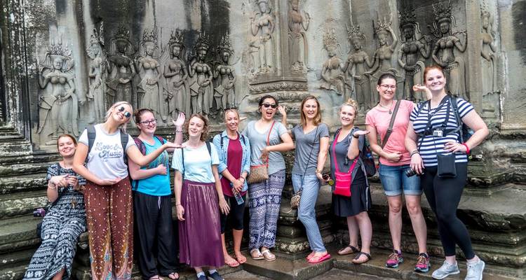 Tour group poses playfully beside intricate Apsara carvings at Angkor Wat.
