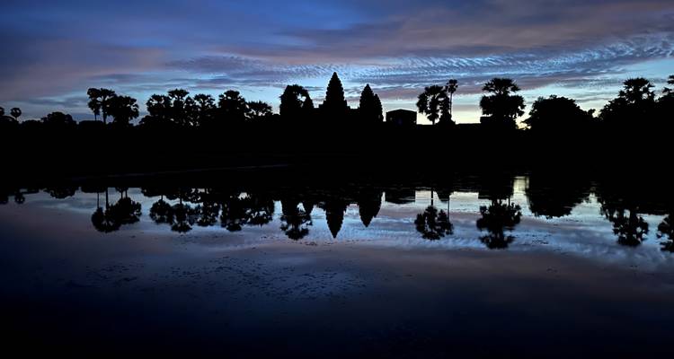 Silhouette of Angkor Wat reflected in still water against a violet predawn sky.
