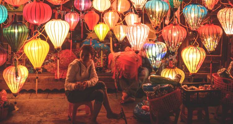 Marché nocturne coloré à Hoi An rempli de lanternes en soie lumineuses et de vendeurs assis parmi des paniers de marchandises.