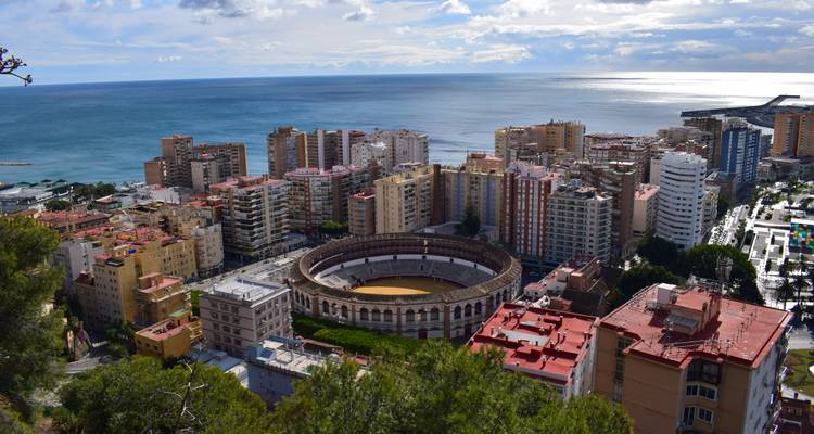 Aerial view of Malaga's circular bullring surrounded by colourful apartment blocks beside the Mediterranean.