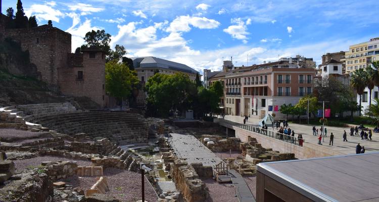 Roman theatre site with modern plaza and visitors exploring amid blue skies in Malaga.