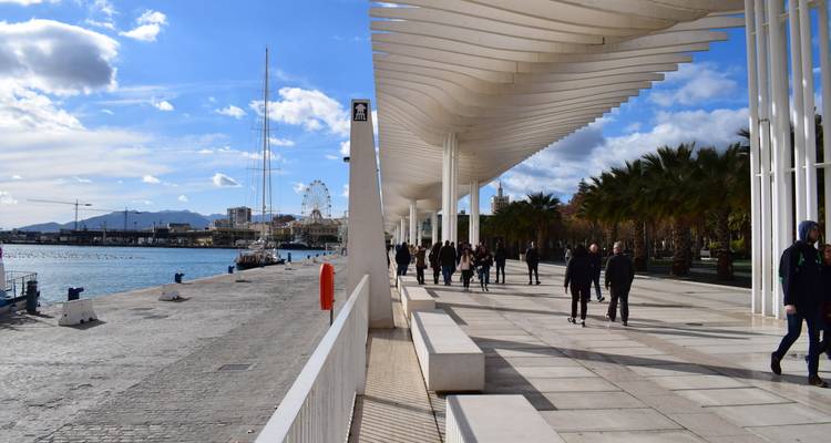 Modern white pergola walkway along Malaga waterfront with people strolling beside the marina.