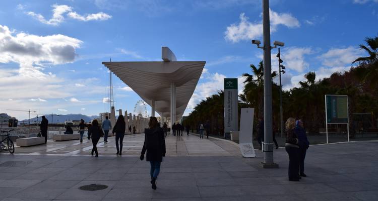Pedestrian promenade at Malaga port with visitors walking beneath a modern canopy beside the water.