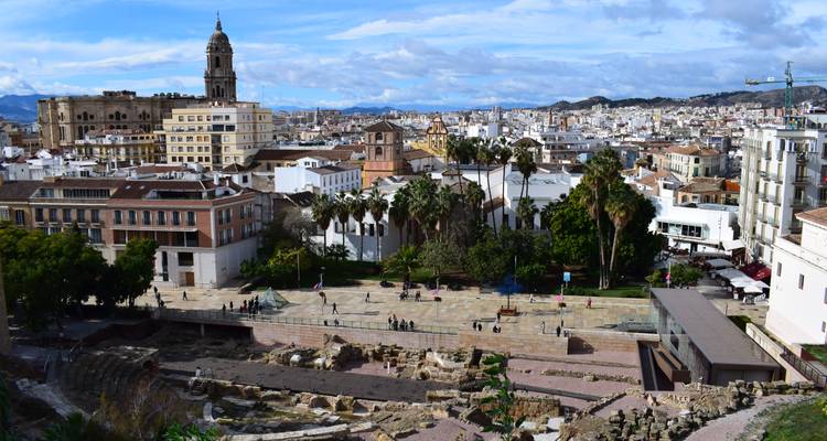 Panoramic cityscape of Malaga with cathedral tower rising above rooftops and mountains in the distance.