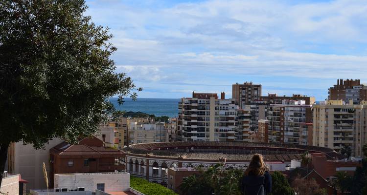 View toward Malaga bullring and sea with a single woman observing from a garden overlook.
