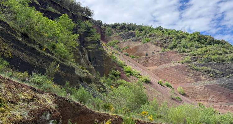 Gekleurde vulkanische rotsen en groene begroeiing onder een gedeeltelijk bewolkte hemel in een robuust natuurpark.
