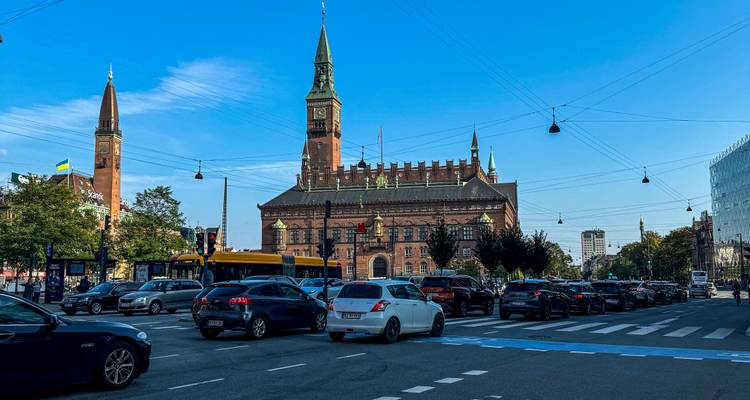 Druk verkeerskruispunt voor het Kopenhagense stadhuis met trams, auto's en fietsers.