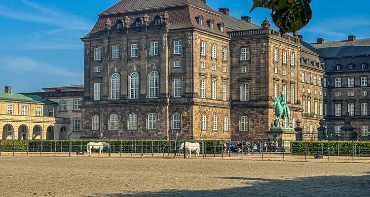 Zijkant van het Christiansborg Palace binnenplein met ruitersculptuur en zandige rijbaan op de voorgrond.