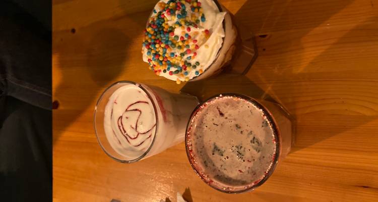Drie kleurrijke toetjesdrankjes op een houten tafel, inclusief slagroom en regenboogsprinkels